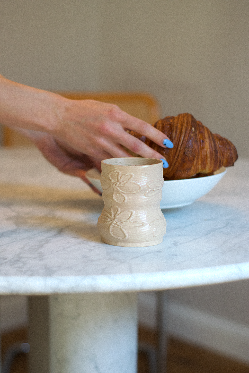 Lifestyle shot of a cashew-colored 3D-printed clay matcha cup by GLINA3, resting on a marble table with a croissant in the background.